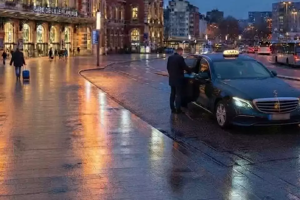 Taxi Lille Le Quesnoy : chauffeur ouvrant la portière d’un taxi devant une gare