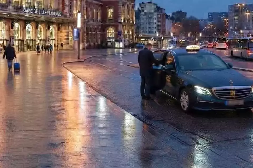 Taxi Lille Sains-du-Nord : chauffeur ouvrant la portière d’un taxi devant une gare